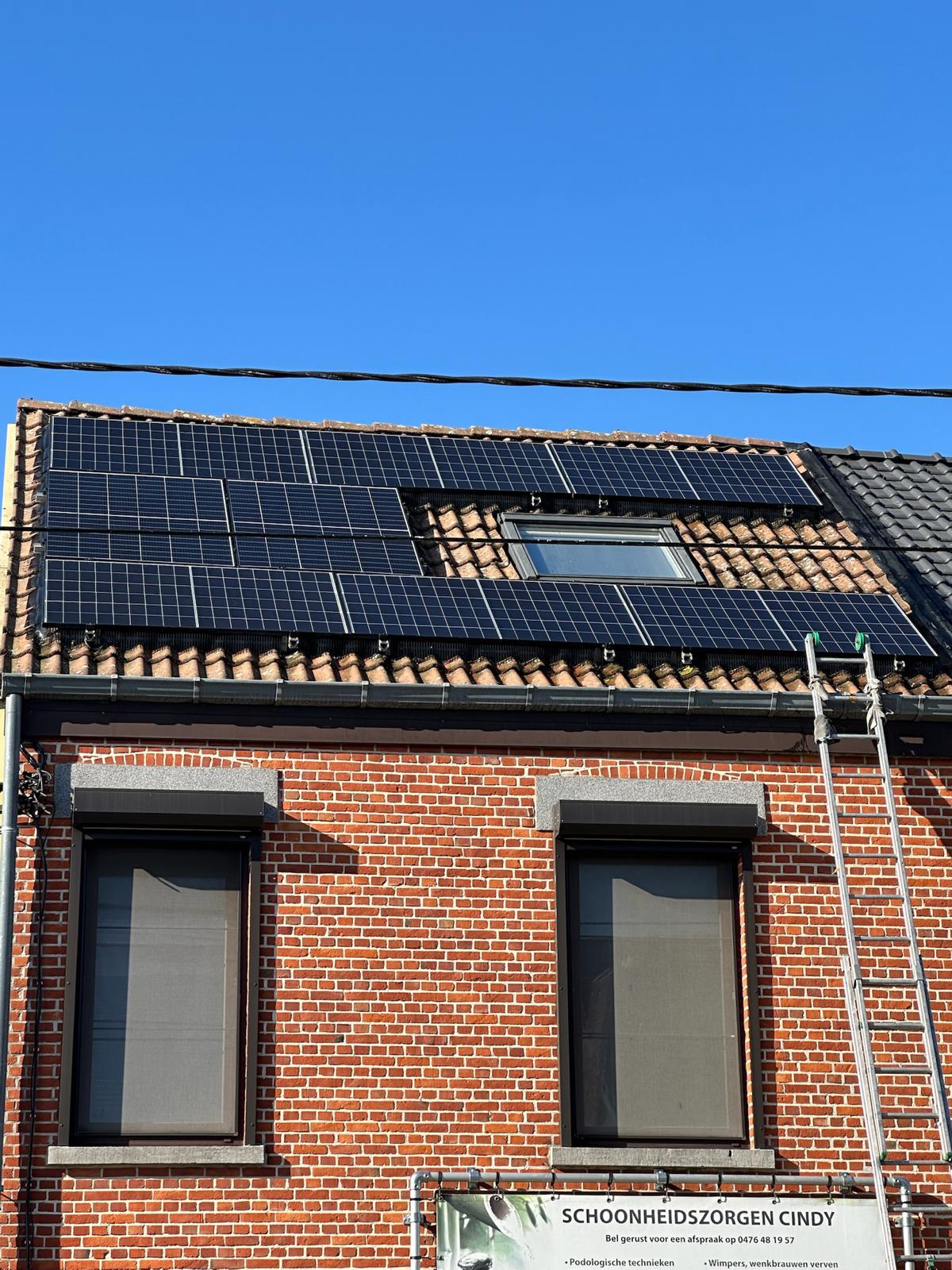 Bakstenen woning met zonnepanelen rond een dakraam, met ladder tegen de dakrand