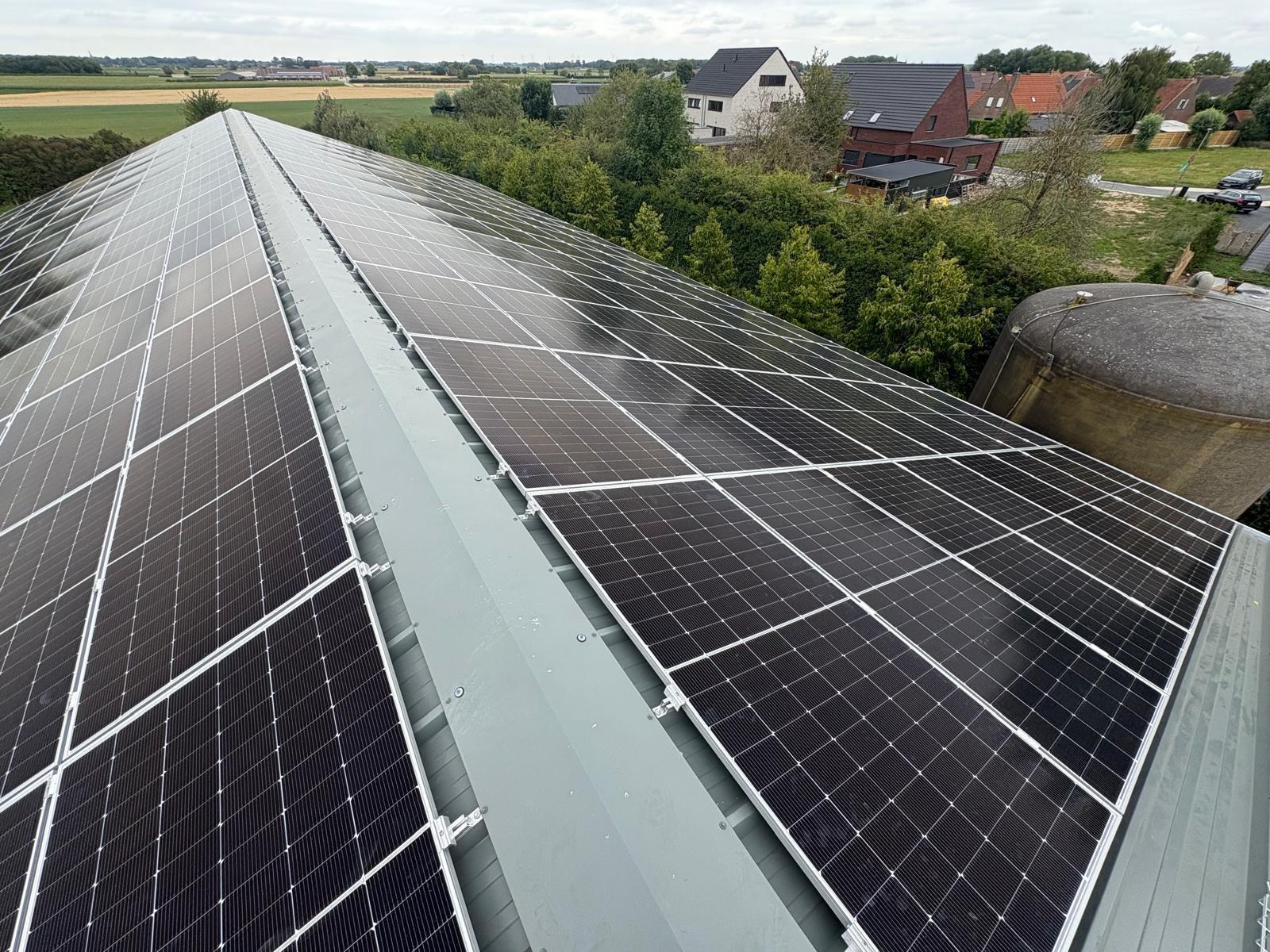 Zonnepanelen op een landelijke loods met velden en woningen op de achtergrond