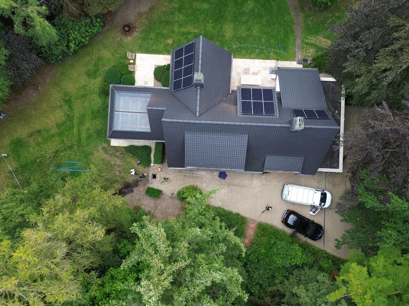 Luchtfoto van een woning met zonnepanelen, omringd door tuin en bomen